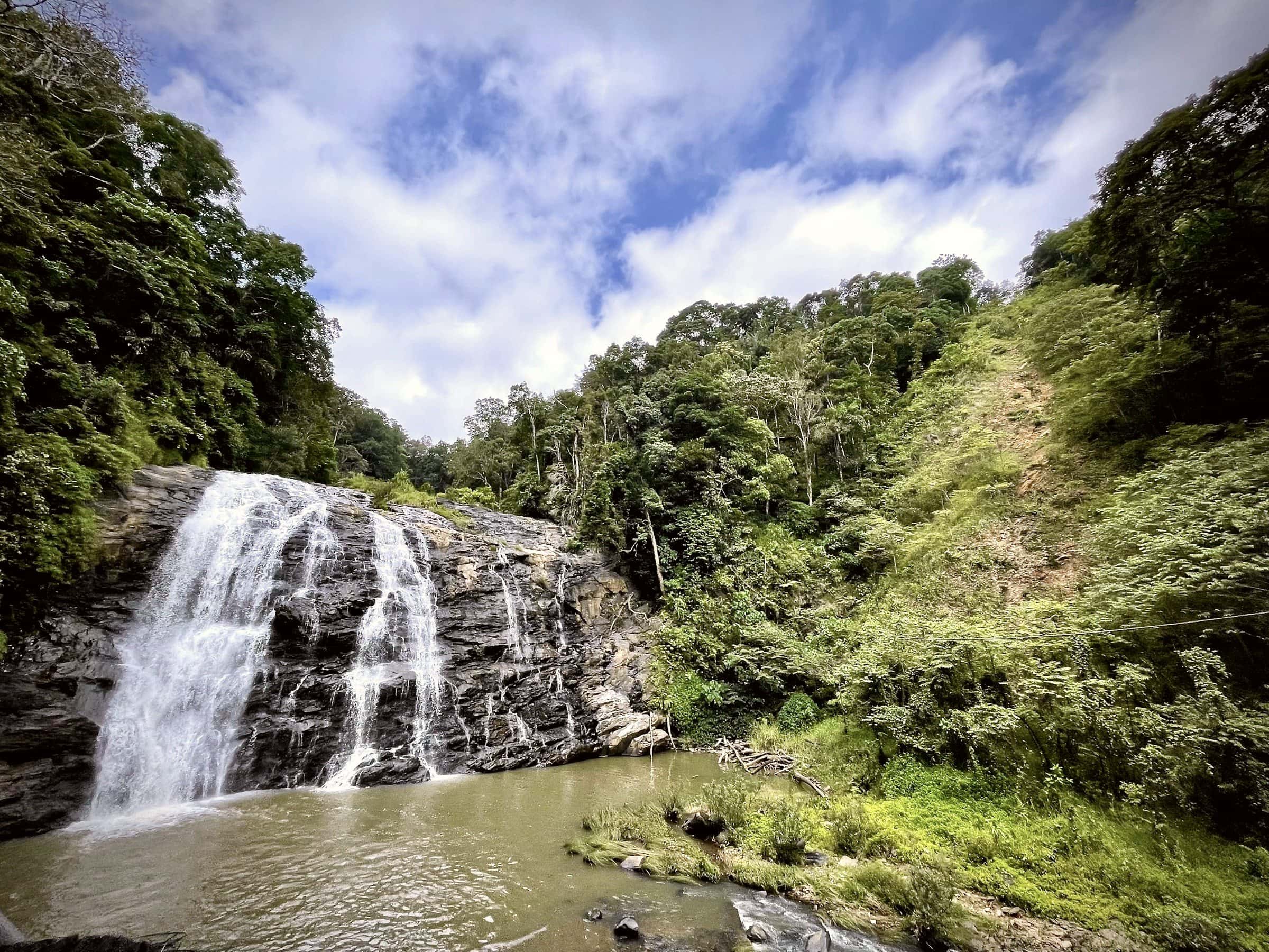 Abbey Falls near Madikeri, pouring over dark rock into a pool below forested slopes