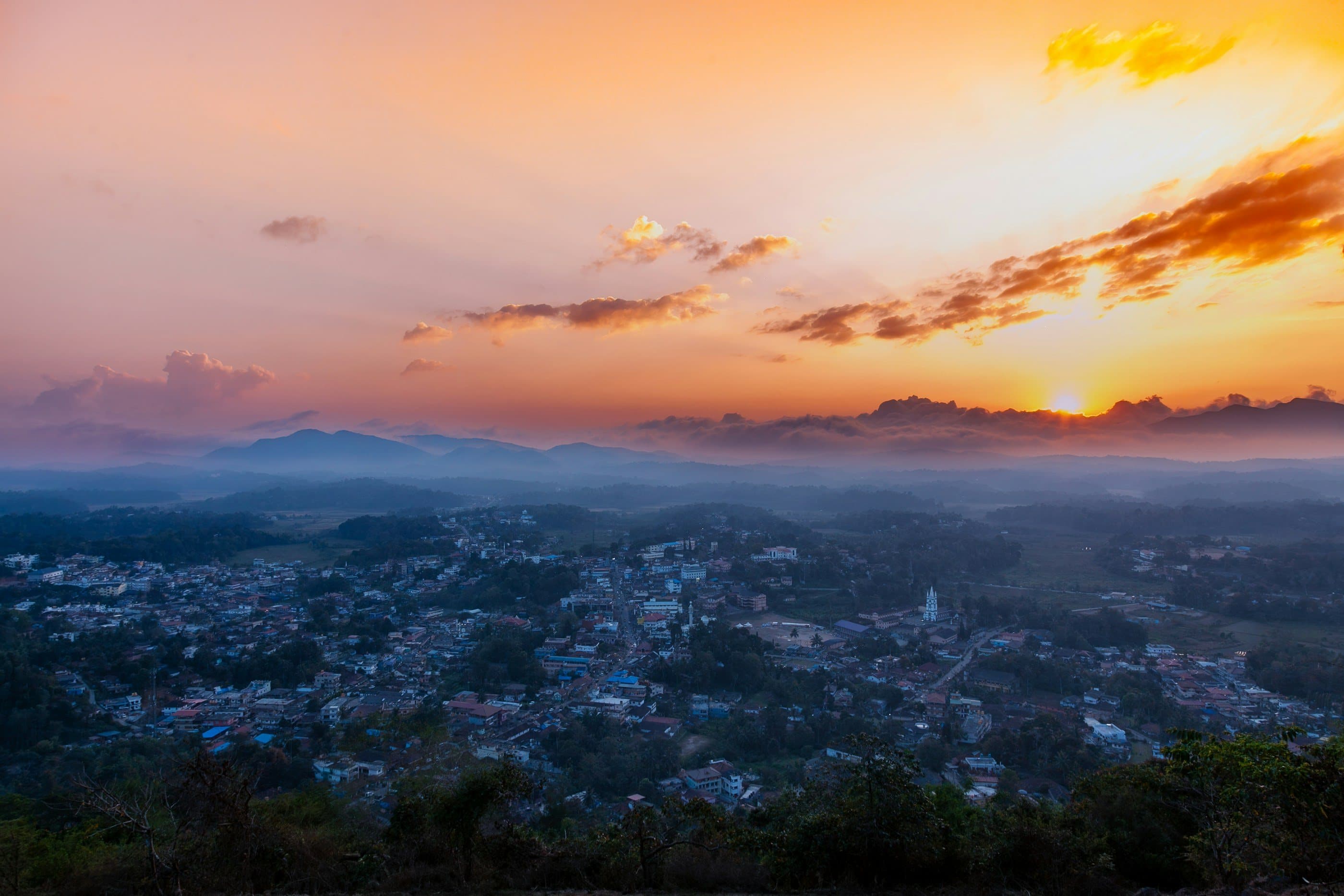 Sunrise over Virajpet, its streets below layers of misty hills and a gold and orange sky